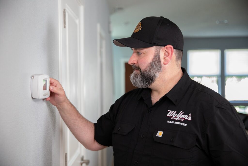 Wolfer's technician checking a thermostat on a home's white wall.